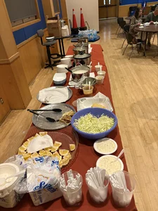 Long buffet table with chafing dishes, lettuce bowls, sauces, lemons; people dining.